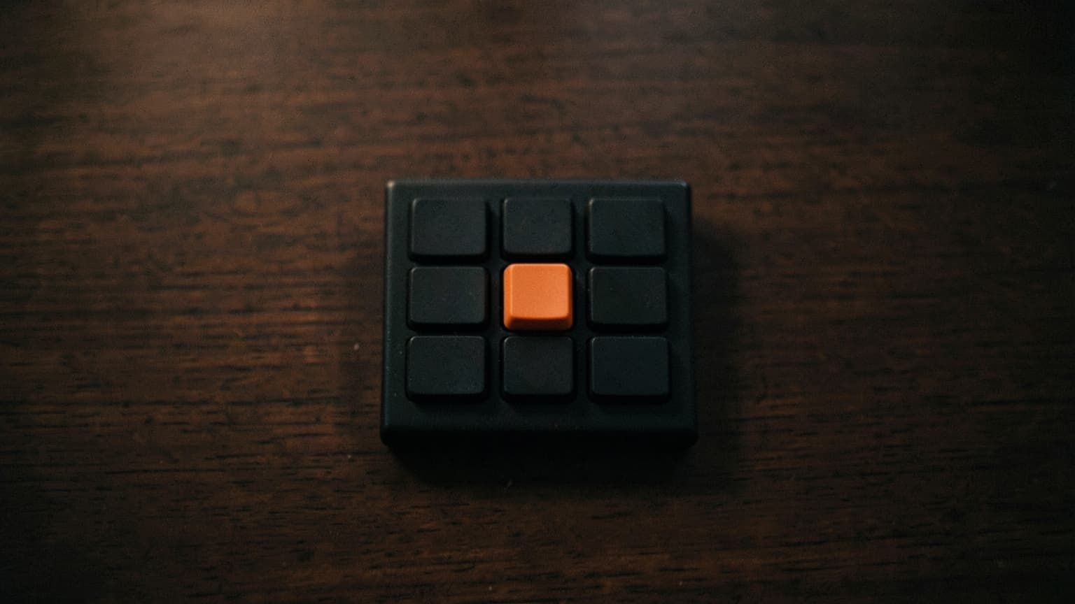 A grid of smooth blank black keys with one orange key pressed lower than the rest