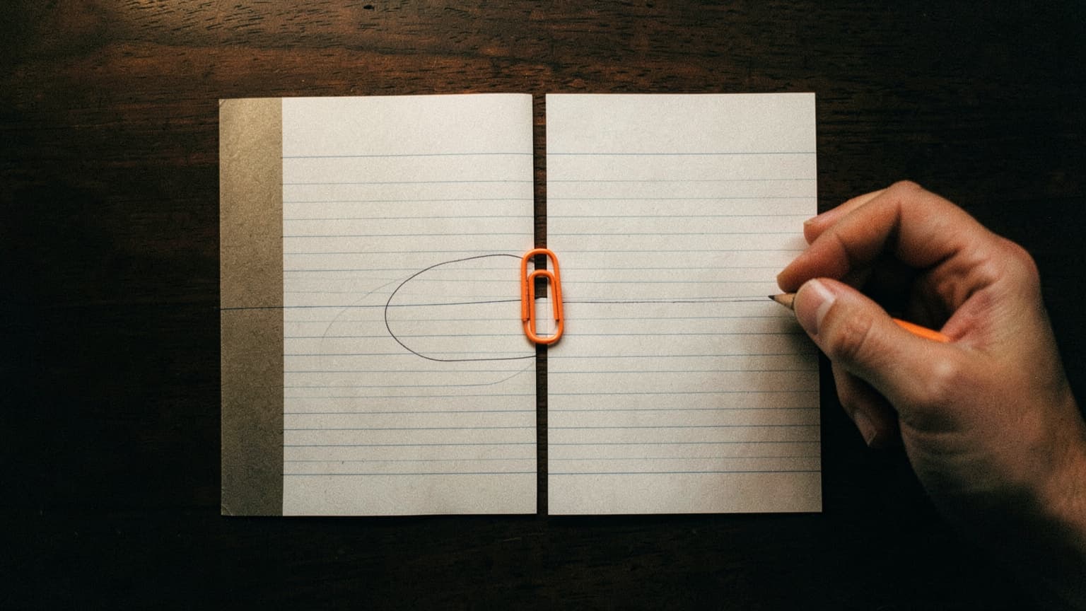 A hand circling one ruled line on a two page scope, held together by a single orange paperclip