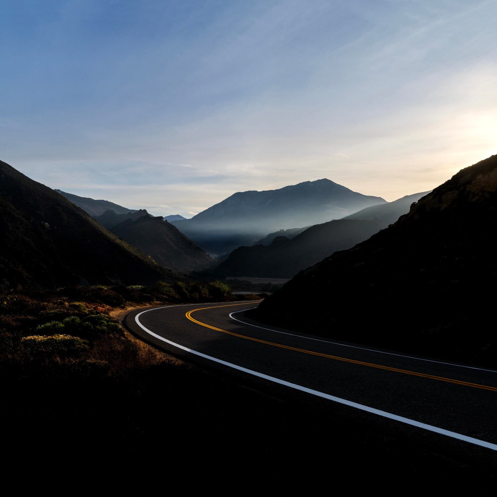 A mountain road curving through dark hills toward a misty valley